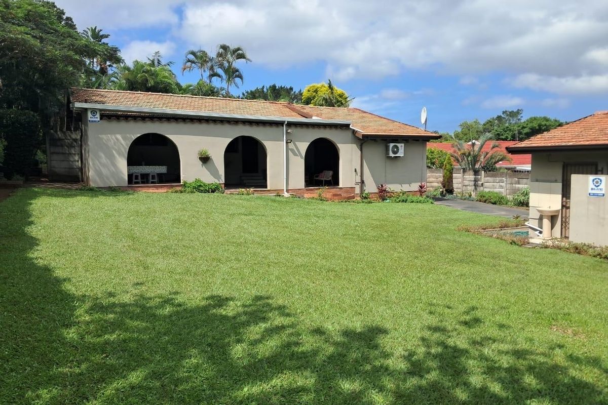 Rear view of the house featuring a spacious lawn, a covered arched patio area, and a well-maintained garden setting.
