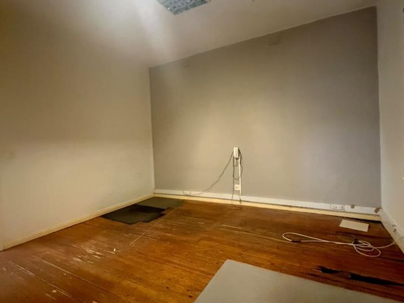 An empty bedroom featuring original timber flooring in need of restoration, a fluorescent light fixture, and a wall-mounted intercom unit.