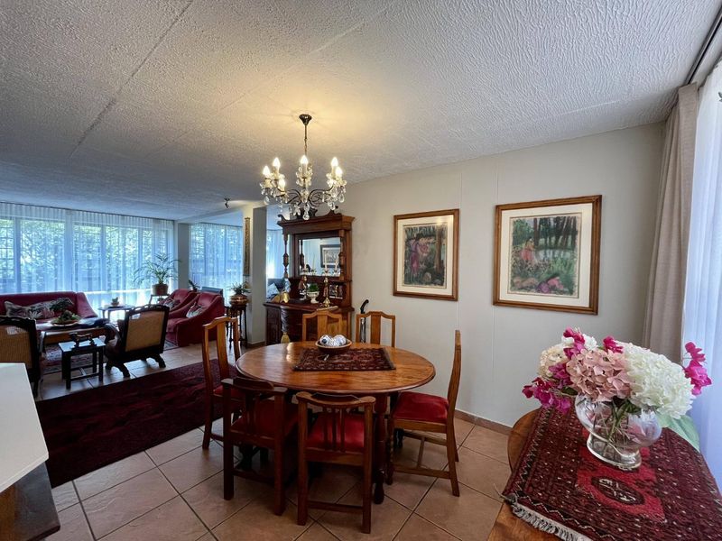 Spacious open-plan living and dining area featuring tiled flooring, a classic chandelier, and large windows providing ample natural light.