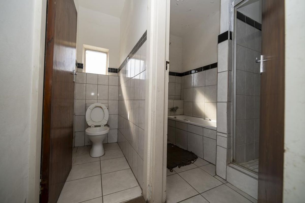 A dated bathroom featuring a separate toilet and a combined bath and shower area with tiled walls and flooring.