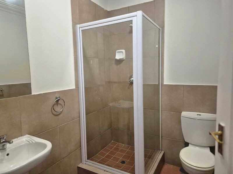 A functional bathroom featuring a shower enclosure, wall-mounted basin, and toilet with neutral wall tiling.