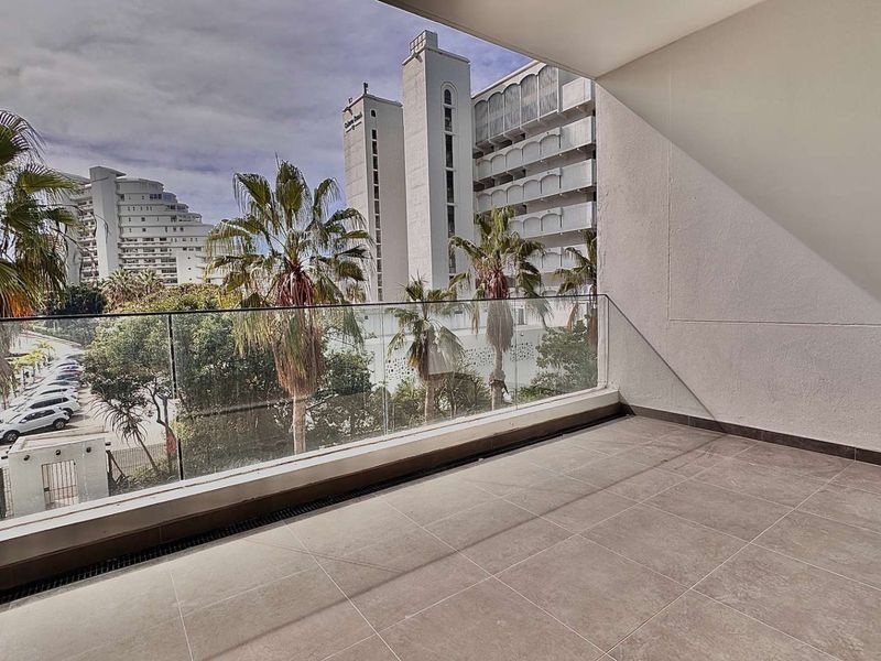 A modern covered balcony featuring sleek glass balustrades and neutral floor tiling, offering an elevated view of the surrounding urban landscape.