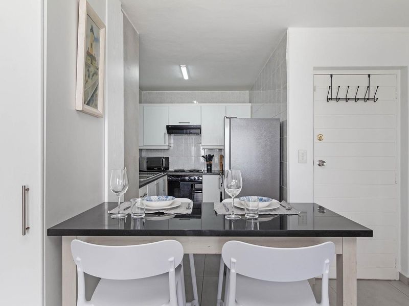 An open-plan kitchen and dining area featuring modern white cabinetry, a sleek black countertop, and tiled finishes throughout.