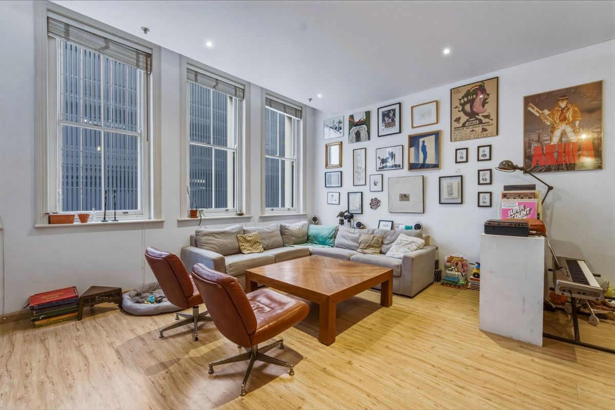 A bright living room featuring timber laminate flooring, recessed downlighting, and large sash windows that provide ample natural light.