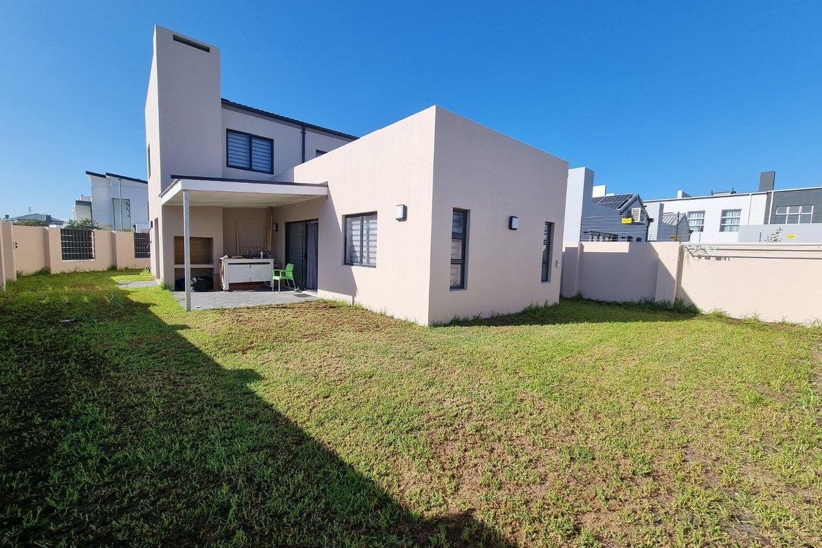 Rear view of a modern double-story house featuring a covered patio with a built-in braai and a spacious private garden.