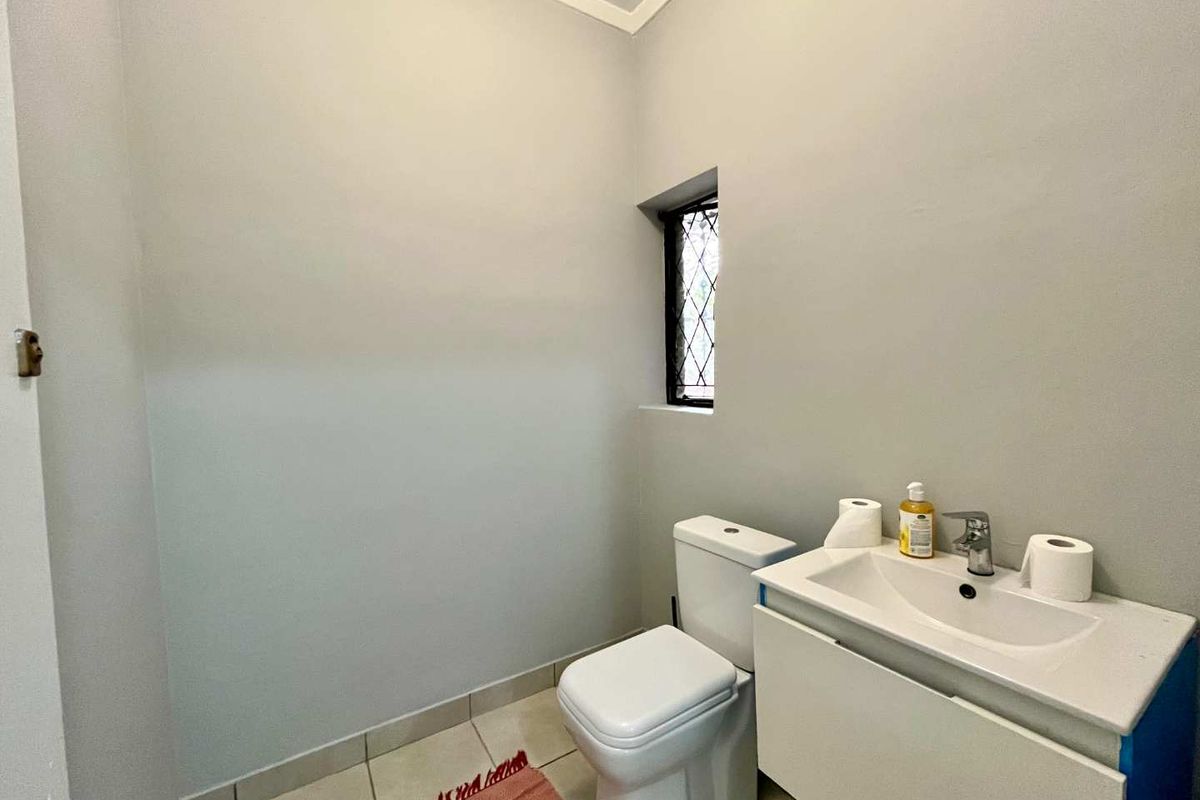 A clean and functional guest bathroom featuring a modern vanity cabinet, white ceramic washbasin, and a small leaded glass window.