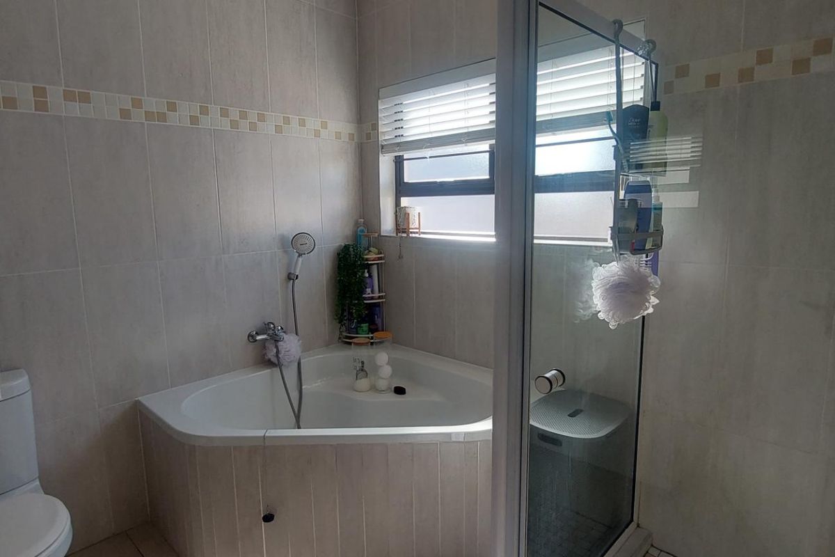 A functional bathroom featuring a corner bathtub, separate shower enclosure, and neutral wall tiling with a decorative border.