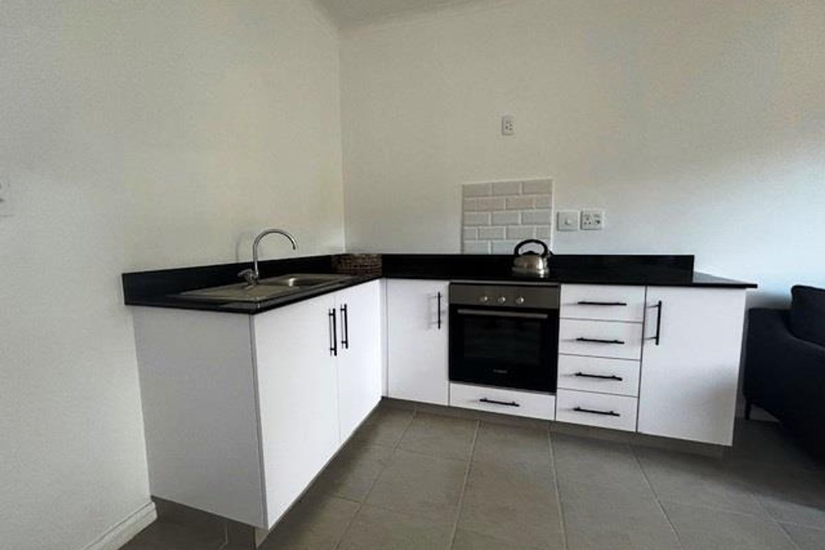 Compact kitchen featuring white cabinetry, black countertops, a built-in oven, and a stainless steel sink with tiled splashback.