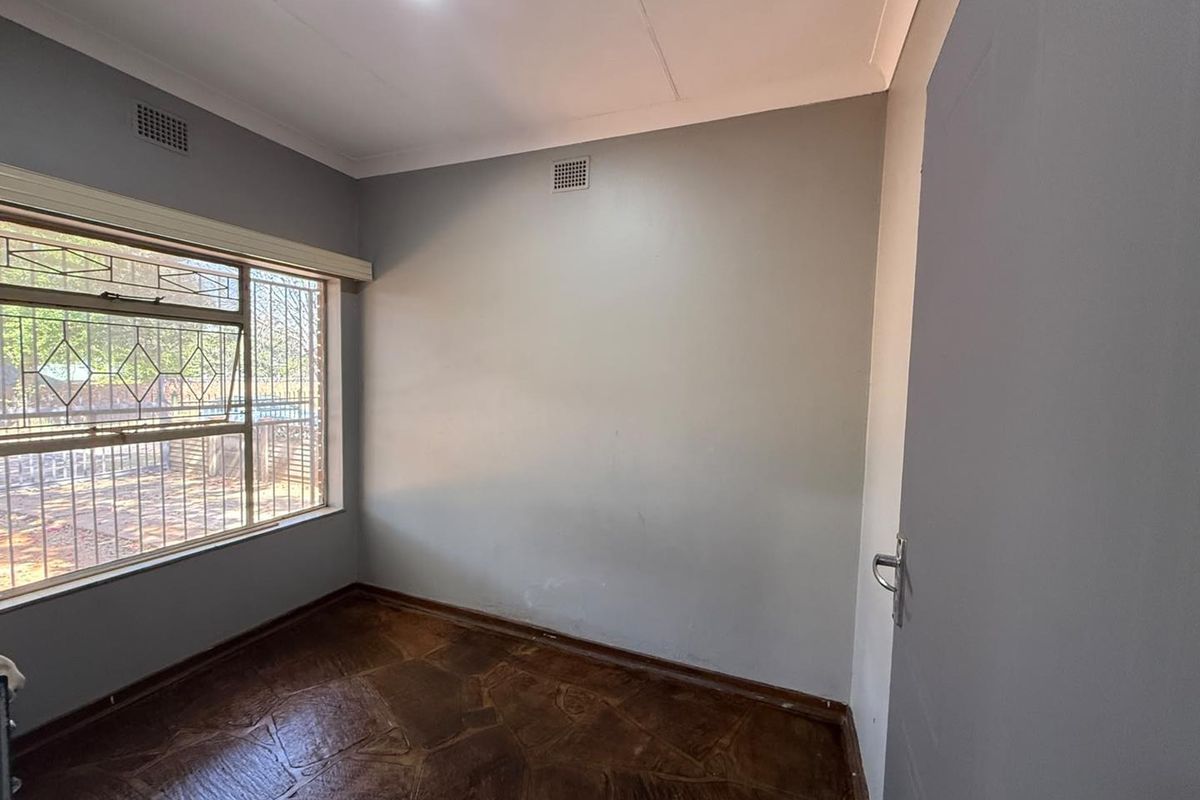 An empty bedroom featuring stone tile flooring, security bars on the window, and neutral grey walls with cove cornicing.