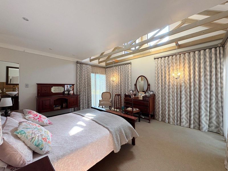 Spacious bedroom featuring exposed timber roof trusses, recessed lighting, and large sliding glass doors with floor-to-ceiling curtains, creating a bright and airy atmosphere.