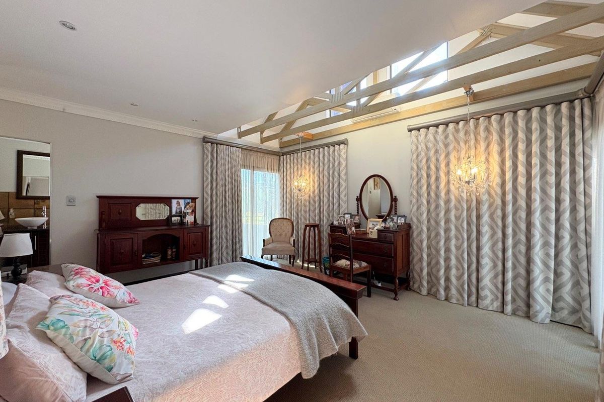 Spacious bedroom featuring exposed timber roof trusses, recessed lighting, and large sliding glass doors with floor-to-ceiling curtains, creating a bright and airy atmosphere.