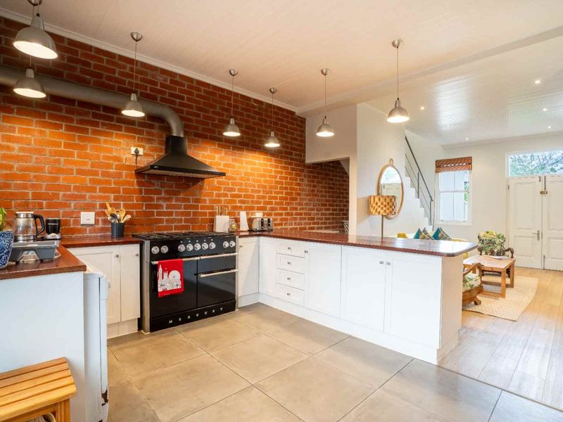 Open-plan kitchen and living area featuring an exposed brick wall, modern white cabinetry, timber countertops, and a professional-style range cooker.