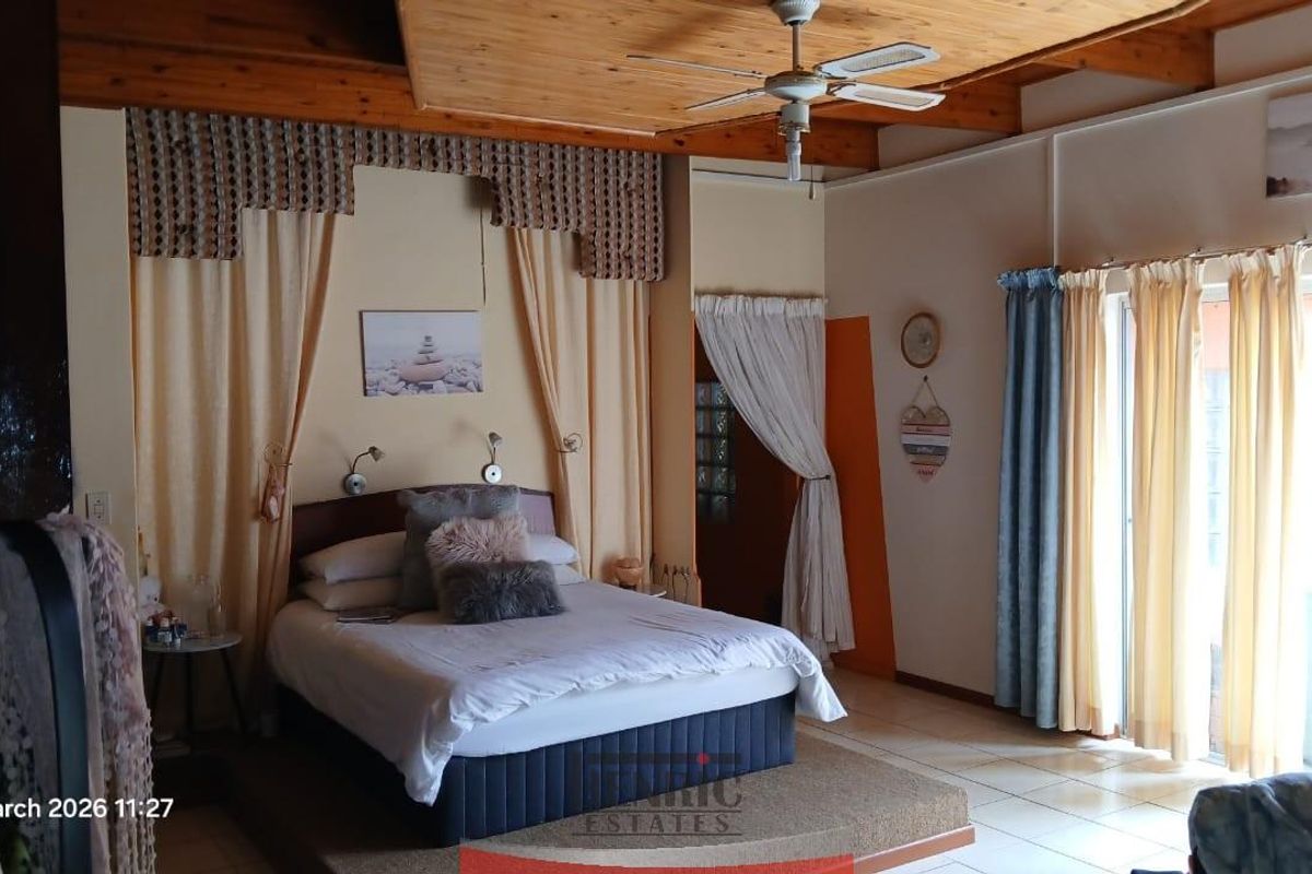 Spacious bedroom featuring a raised platform bed area, exposed timber ceiling beams, and sliding glass doors providing access to the exterior.