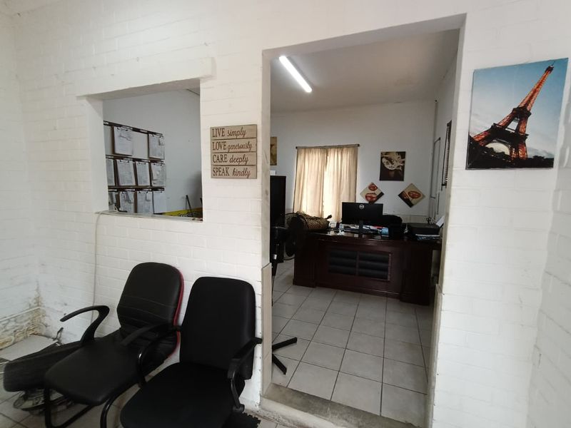 An office space featuring painted brick walls, ceramic tile flooring, and a convenient pass-through window connecting to an adjacent work area.