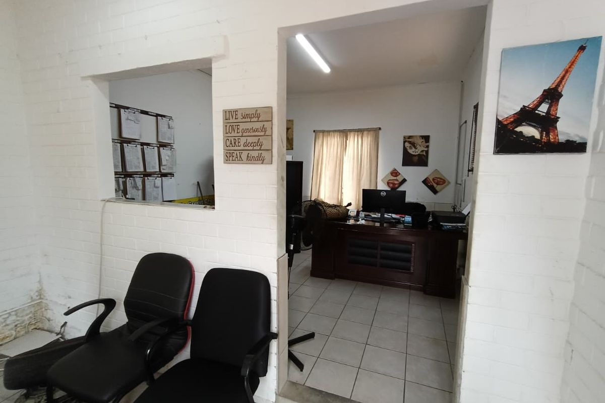 An office space featuring painted brick walls, ceramic tile flooring, and a convenient pass-through window connecting to an adjacent work area.