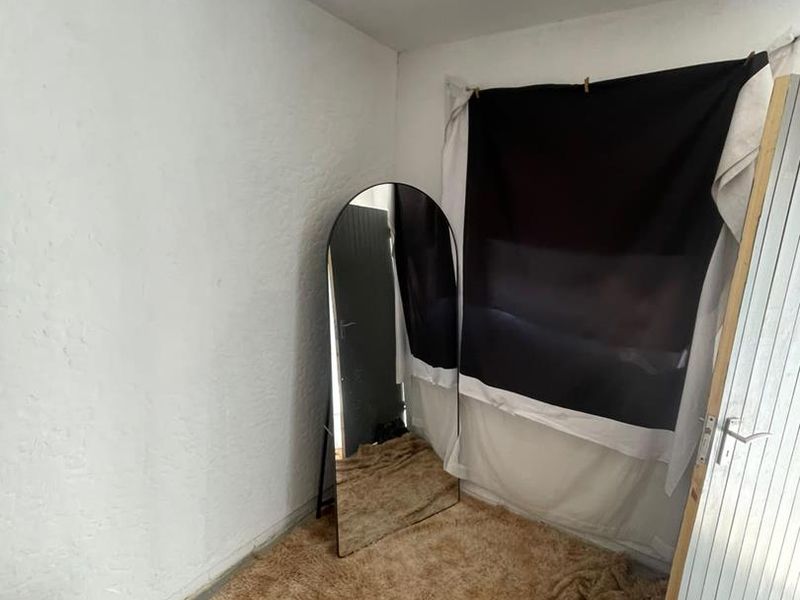 A small, sparsely furnished bedroom space with plain white walls and tiled flooring, requiring cosmetic updates to improve its overall appeal.
