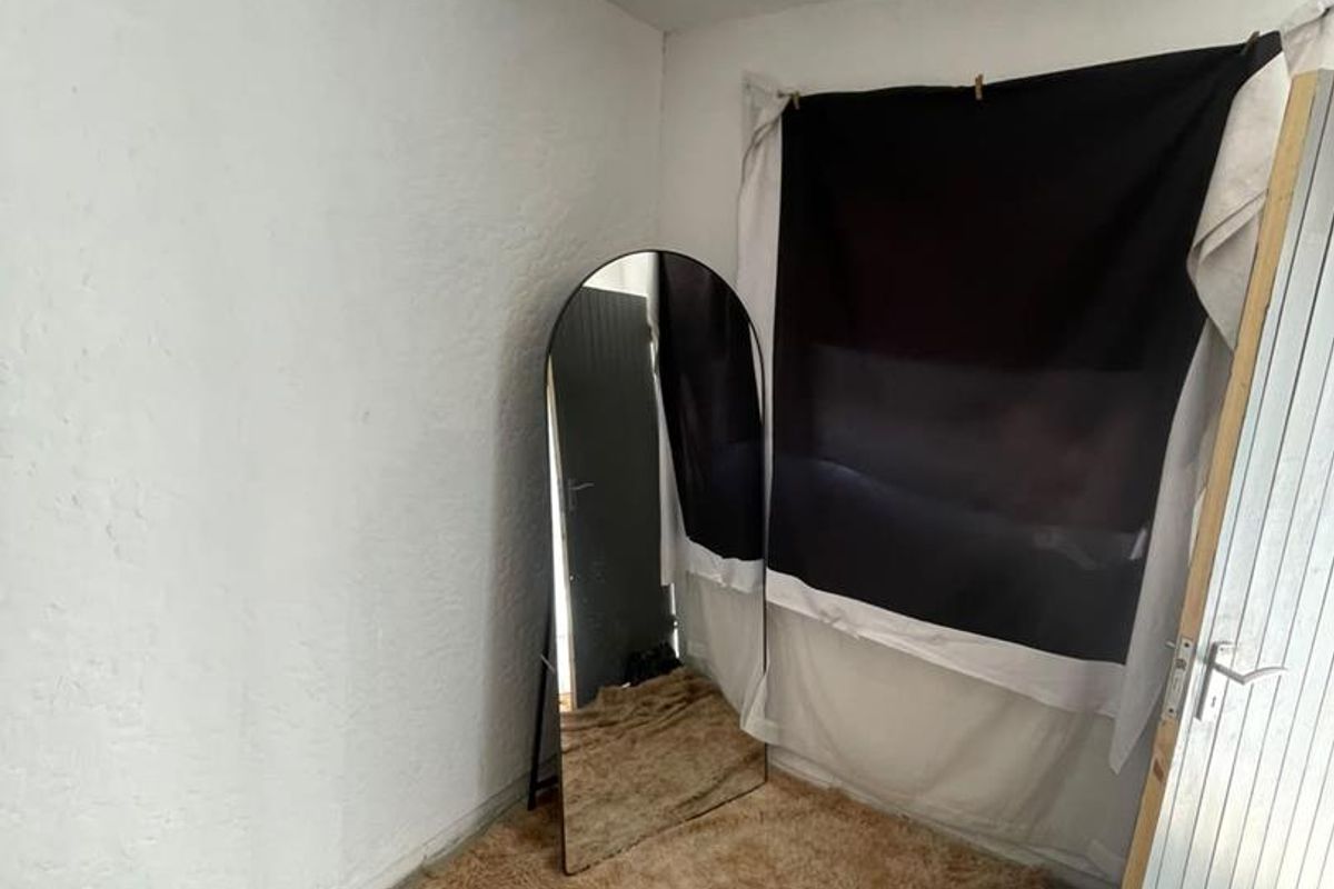 A small, sparsely furnished bedroom space with plain white walls and tiled flooring, requiring cosmetic updates to improve its overall appeal.