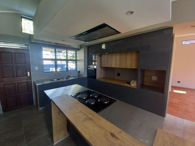 Modern kitchen featuring sleek grey cabinetry, wood-tone accents, a central island with a built-in hob, and high-quality finishes throughout.