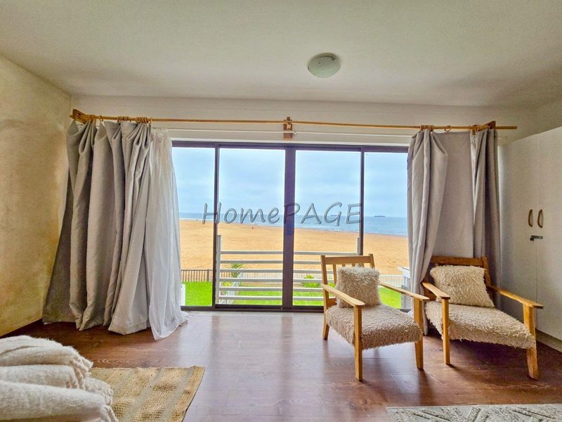 Living room featuring large sliding glass doors with direct beach views, laminate flooring, and neutral wall finishes.
