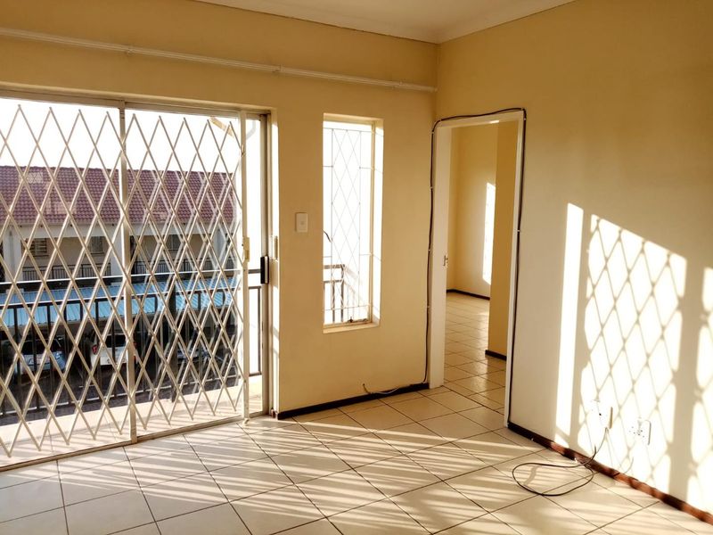 An empty living area featuring tiled flooring, a sliding glass door with security gate, and natural light, leading into an adjacent room.