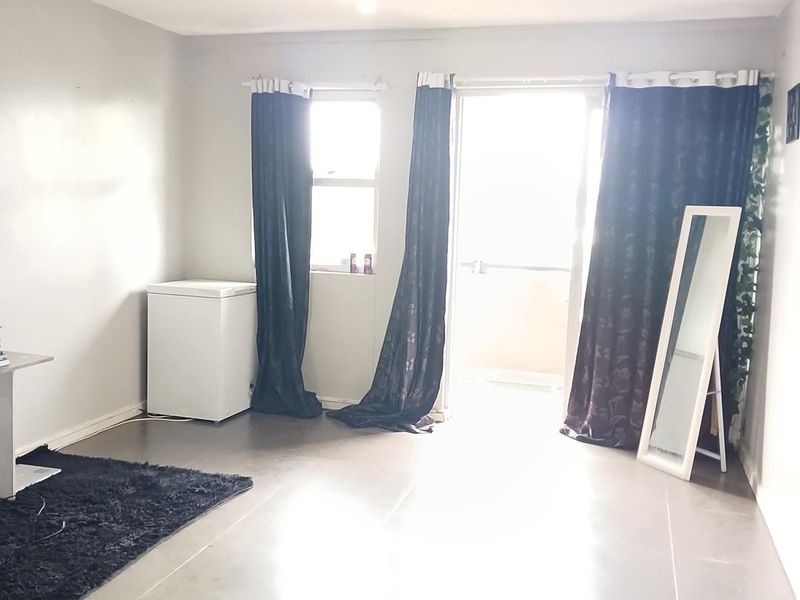 A living room area featuring large format floor tiles, a sliding glass door leading to a balcony, and a window with dark curtains.