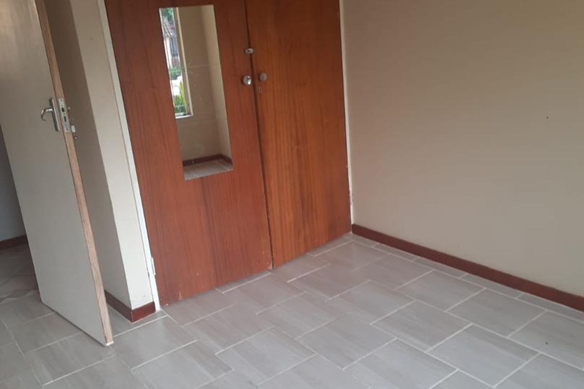 An empty bedroom featuring light-toned tiled flooring and wooden built-in cupboards with integrated mirror panel.
