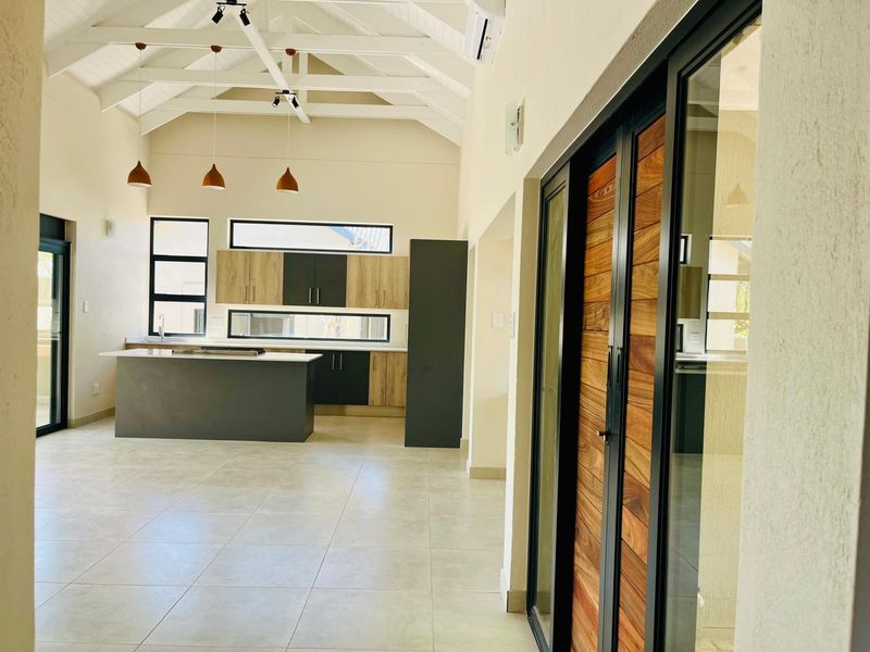 Spacious open-plan living and kitchen area featuring vaulted ceilings with exposed trusses, modern cabinetry, a central island, and large sliding doors leading outdoors.