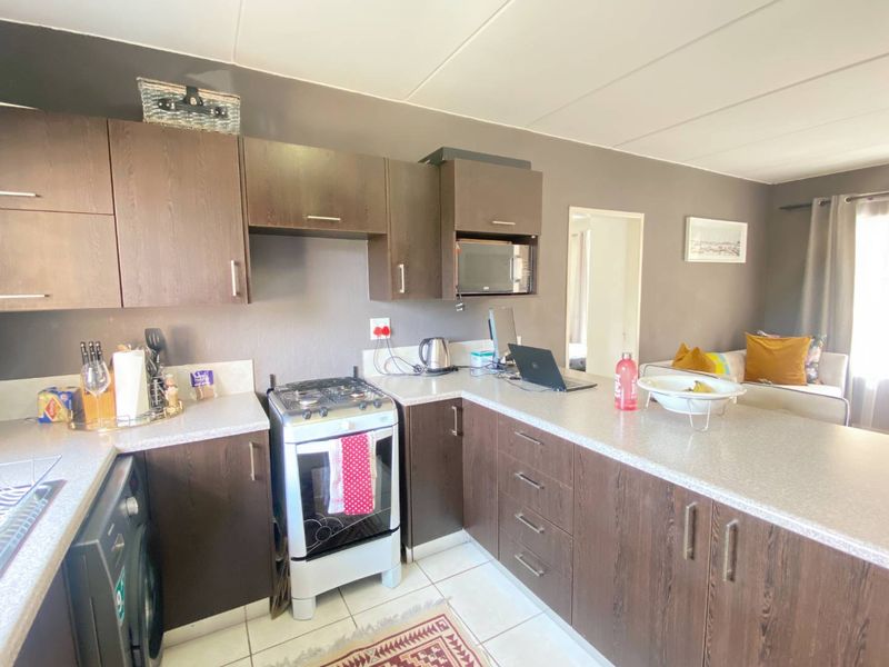 Open plan kitchen featuring dark wood cabinetry, gas stove, oven, and laminate countertops, seamlessly flowing into the adjacent living area.