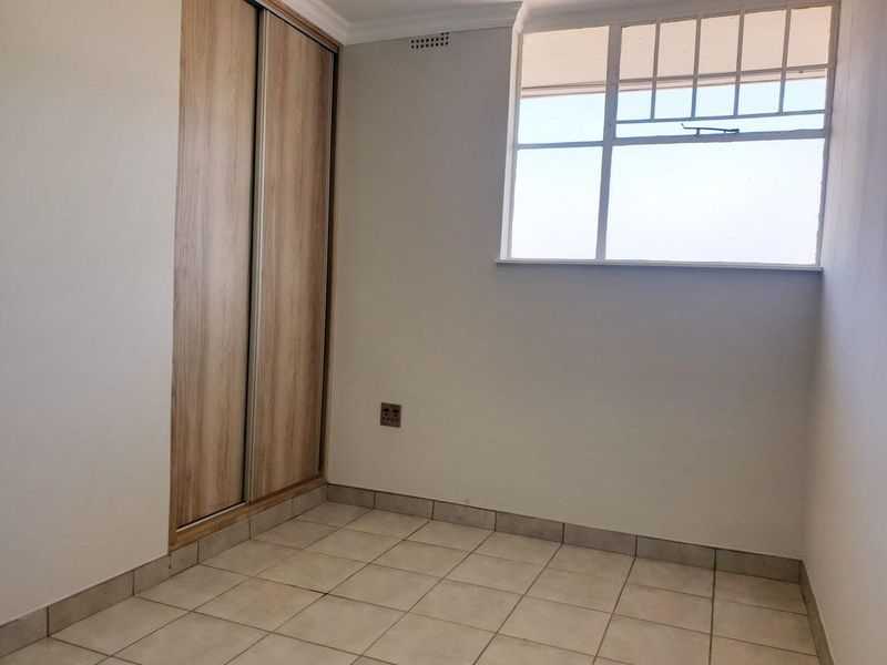 A clean, empty bedroom featuring tiled flooring, a built-in wardrobe with wood-finish sliding doors, and a window with security bars.