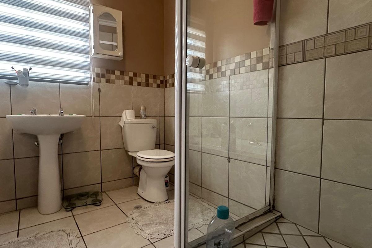A functional bathroom featuring a pedestal basin, a standard toilet, and a glass-enclosed shower with tiled walls and flooring.