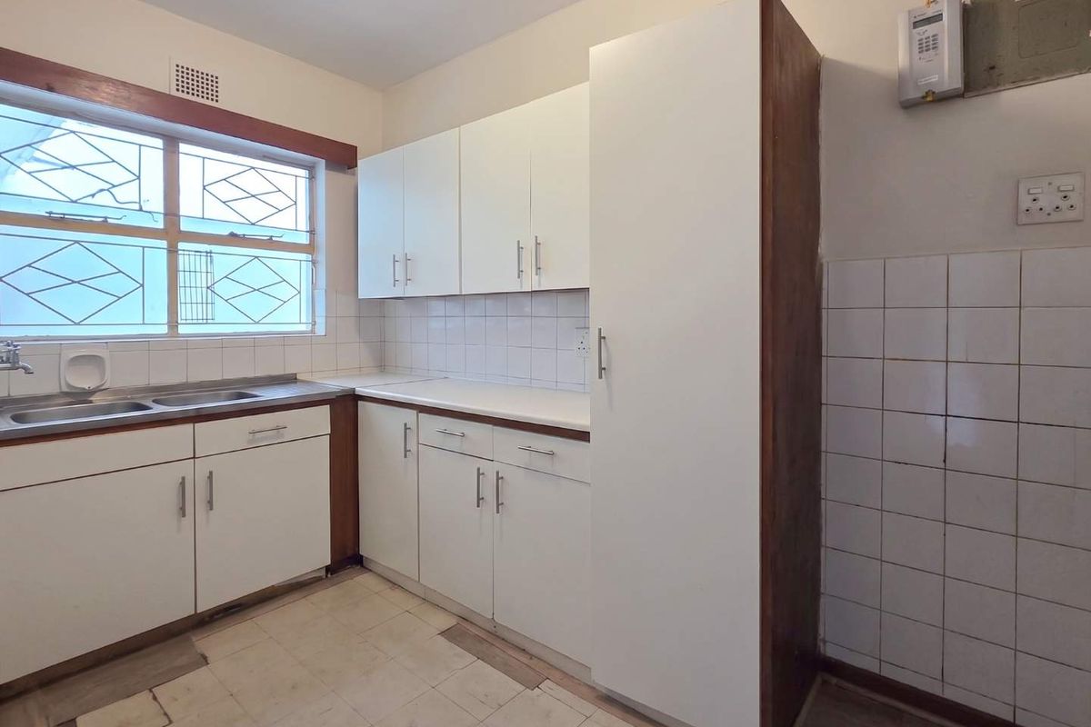 A functional, empty kitchen featuring white built-in cabinetry, laminate countertops, a stainless steel sink, and tiled backsplash, ready for modernization.