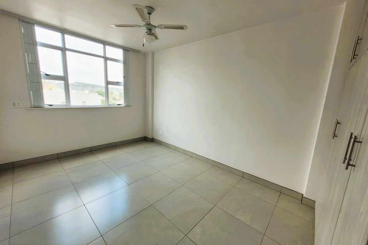 A bright, empty bedroom featuring neutral floor tiles, a ceiling fan, and built-in cupboards, offering a clean and versatile living space.