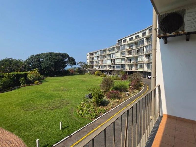 A balcony overlooking a large communal garden and apartment complex, featuring tiled flooring and a metal safety railing.