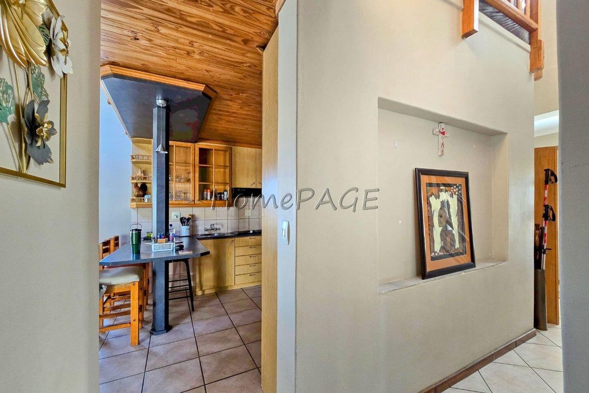 A view from a hallway into a kitchen area featuring wooden ceilings, tiled floors, and built-in cabinetry with a breakfast bar.