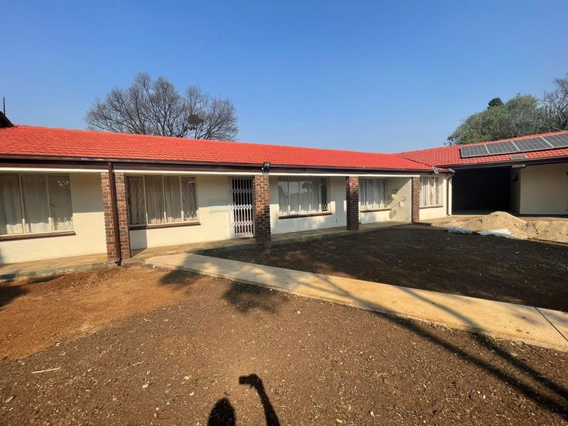 Rear view of the cluster property featuring a red tiled roof, brick pillars, and an unlandscaped garden area with a concrete walkway.