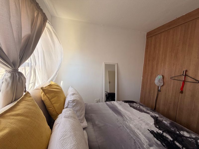A cozy bedroom featuring a built-in wooden wardrobe and natural light from the adjacent window.