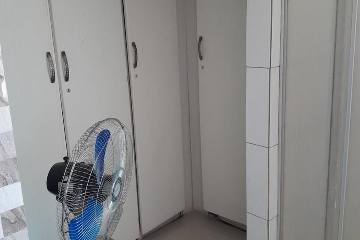 A functional bathroom featuring built-in storage cupboards, a shower enclosure, and neutral wall and floor tiling.