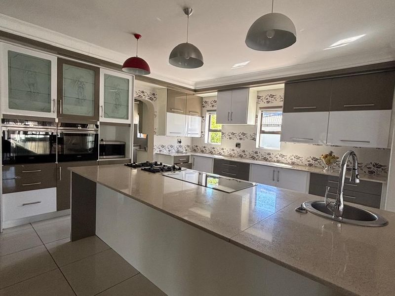 Modern kitchen featuring a large central island with stone countertops, built-in oven, gas hob, and ample cabinetry, finished with tiled flooring.