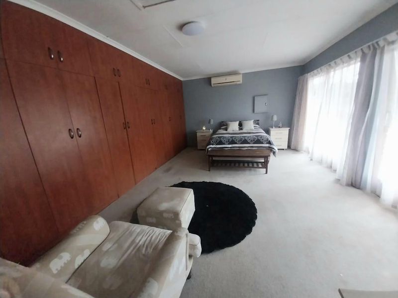 Spacious bedroom featuring extensive built-in wooden cupboards, wall-mounted air conditioning, and large windows allowing for ample natural light.