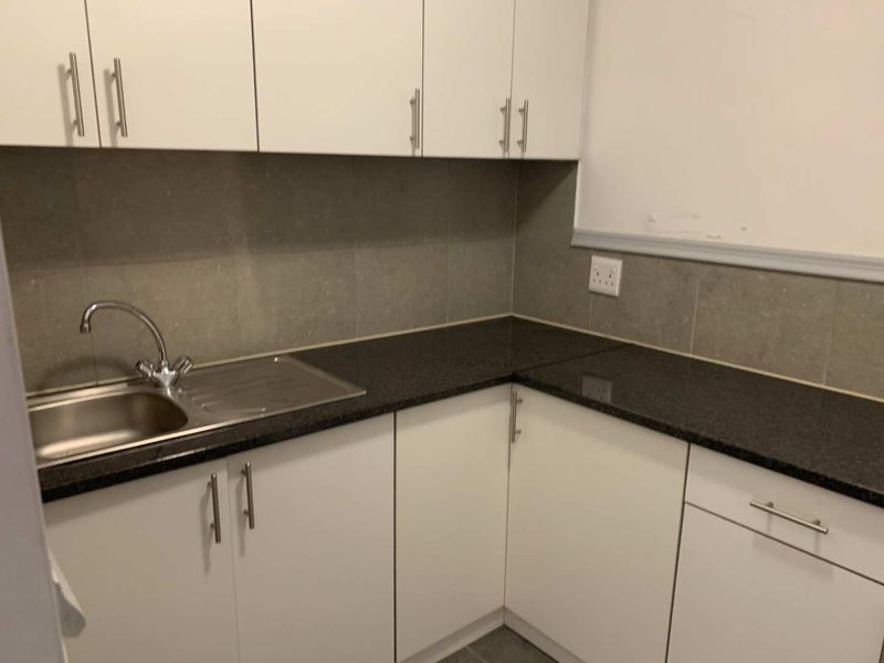 A compact kitchen area featuring white cabinetry, dark granite countertops, and a stainless steel sink with a modern mixer tap.