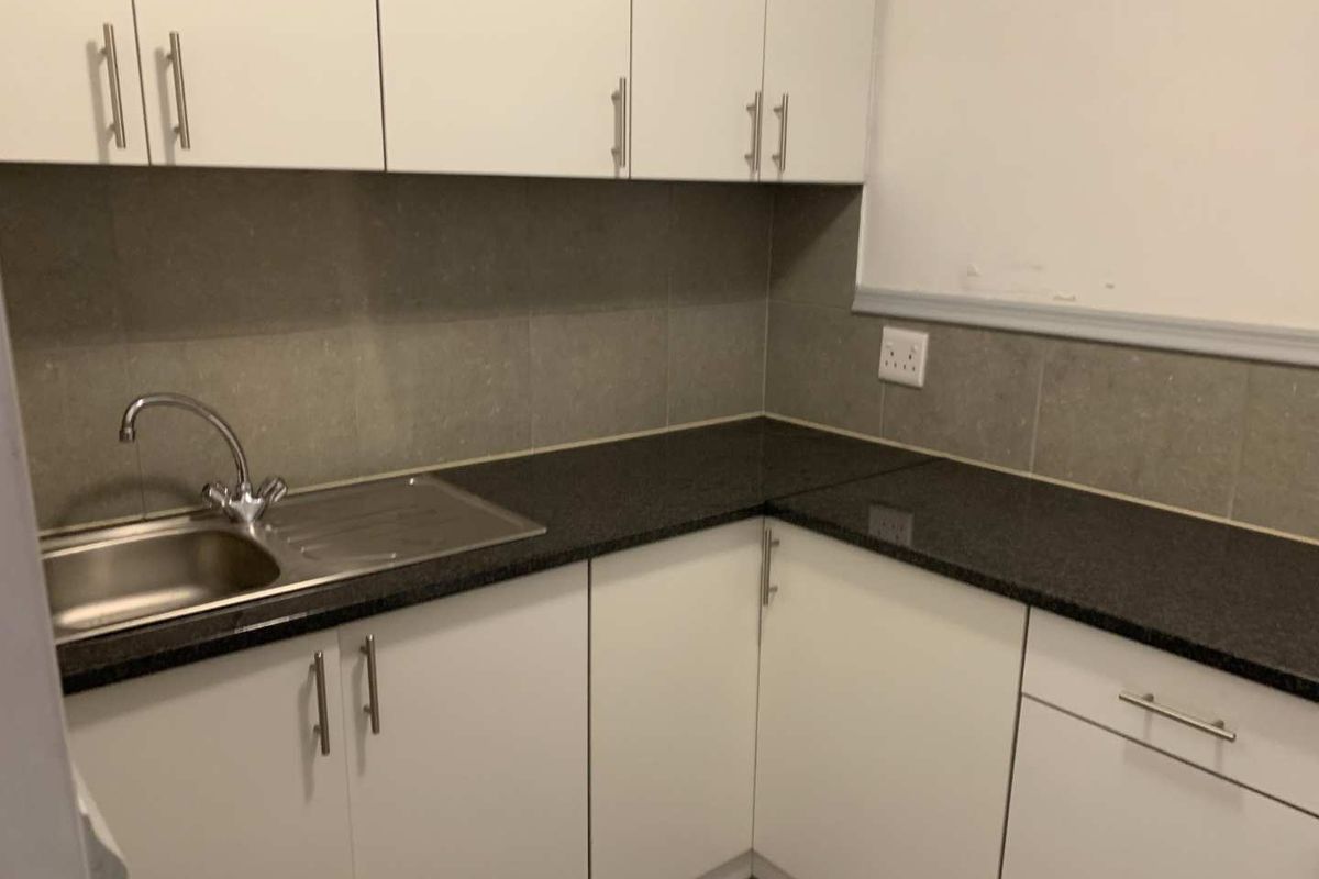 A compact kitchen area featuring white cabinetry, dark granite countertops, and a stainless steel sink with a modern mixer tap.