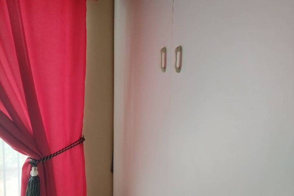 A bedroom interior featuring built-in white cupboards with simple hardware, positioned next to a window with red curtains.