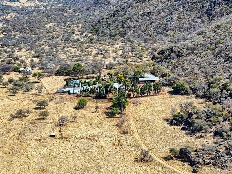 Aerial view of a rural small holding property situated in a mountainous landscape with surrounding dry veld and established trees.