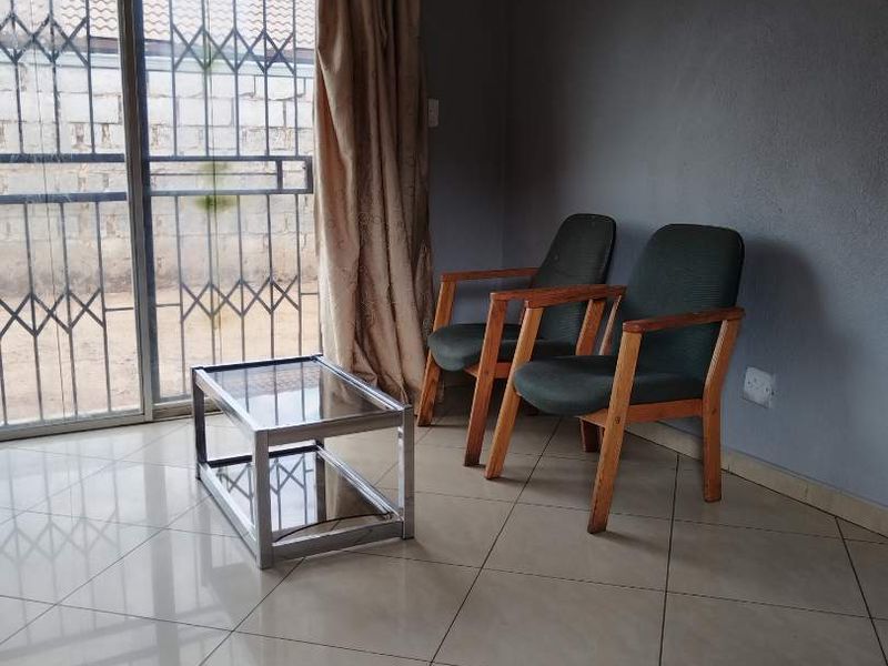 A living area featuring neutral tiled flooring and a sliding glass door with integrated security gate, providing access to the exterior.
