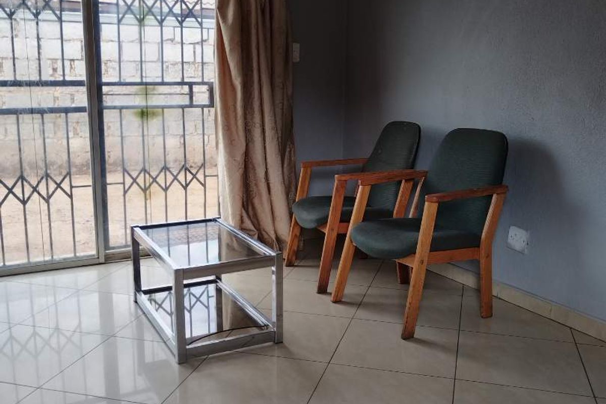 A living area featuring neutral tiled flooring and a sliding glass door with integrated security gate, providing access to the exterior.