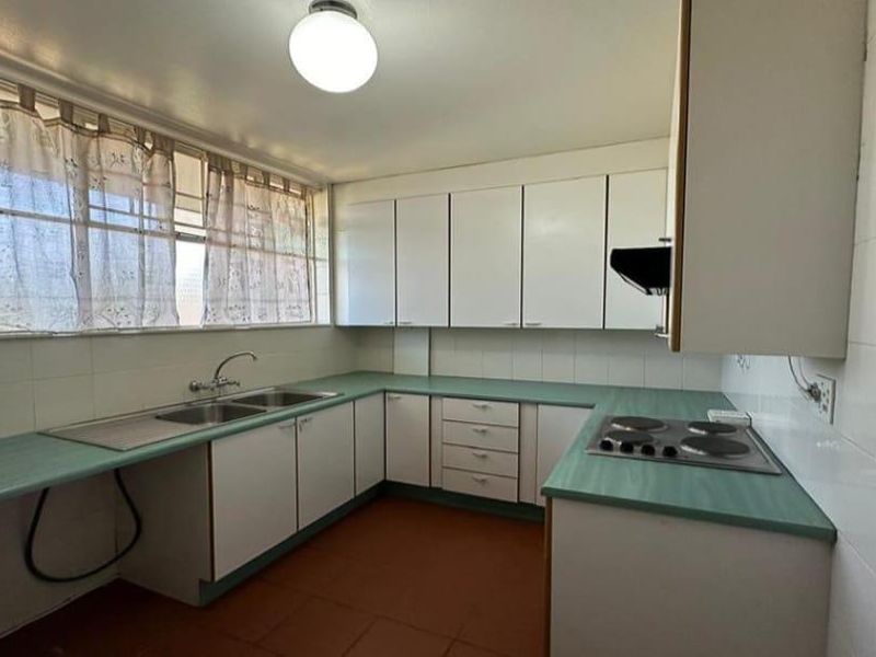 A functional kitchen featuring white cabinetry, green laminate countertops, a double basin sink, and a built-in electric hob with an extractor fan.