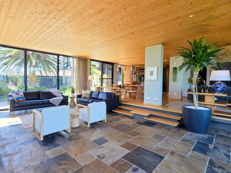 Spacious open-plan living area featuring a warm timber-clad ceiling, natural slate tile flooring, and expansive floor-to-ceiling glass doors leading to the outdoors.