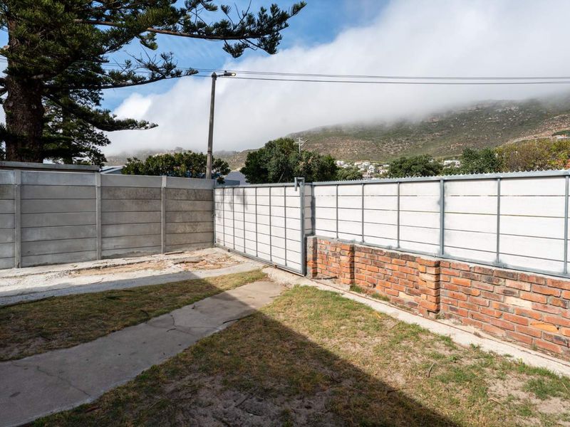 A rear garden area featuring a mix of precast concrete and brick boundary walls, a sliding gate, and a concrete pathway.