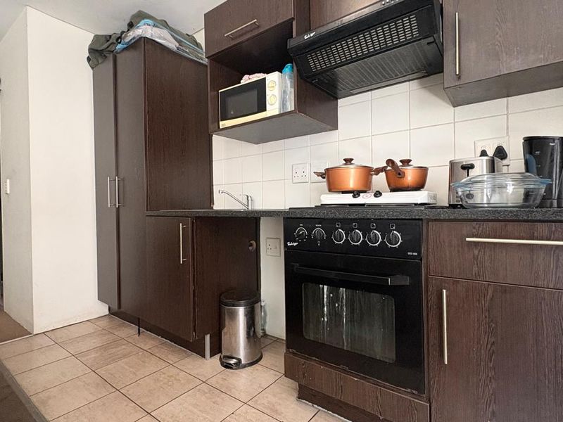 Compact kitchen featuring dark wood cabinetry, built-in oven with hob, extractor fan, and tiled backsplash, providing a functional cooking space.