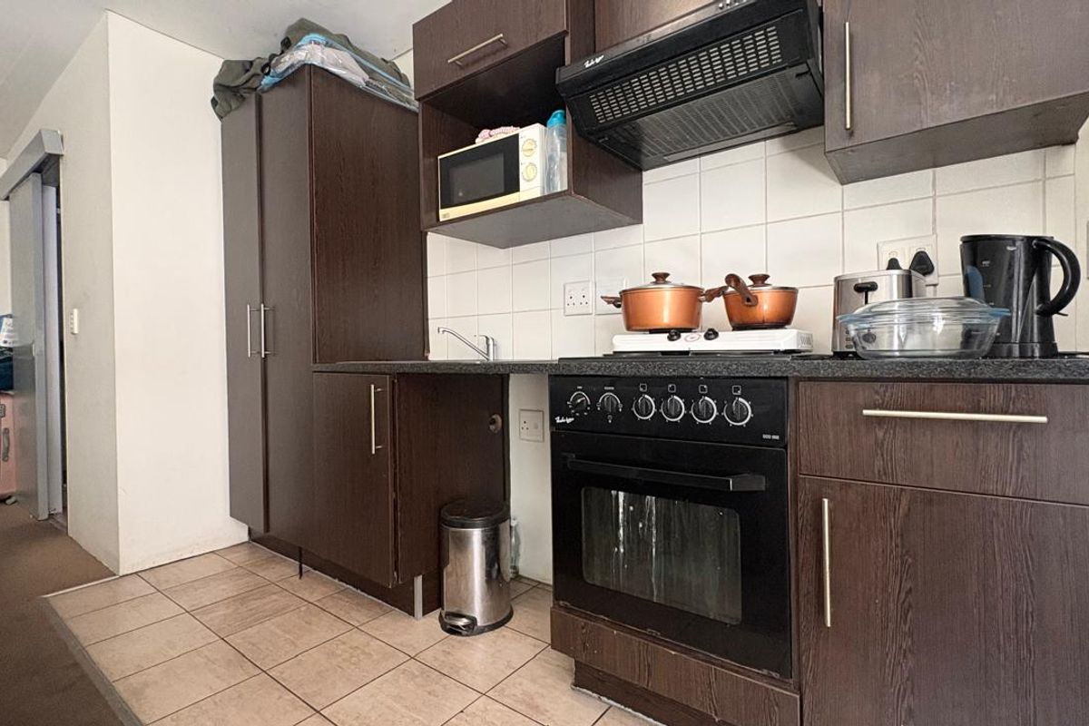 Compact kitchen featuring dark wood cabinetry, built-in oven with hob, extractor fan, and tiled backsplash, providing a functional cooking space.